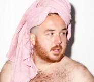 Scottee, shirtless, wearing a pink towel on his head