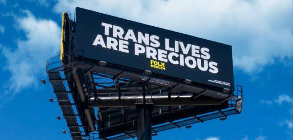 Three billboards in a triangle formation. The front one is visible and reads: Trans lives are precious
