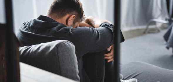 back view of man with panic attack crying and hugging legs in apartment