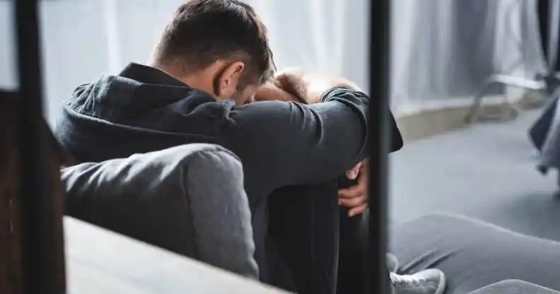 back view of man with panic attack crying and hugging legs in apartment