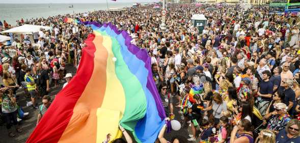 A crowd of pride goers with a giant, long rainbow banner stretching through the crowd