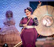 Lawrence Chaney, a drag queen in a long purpler dress with racing flag tripe down the sides, holding a sceptre