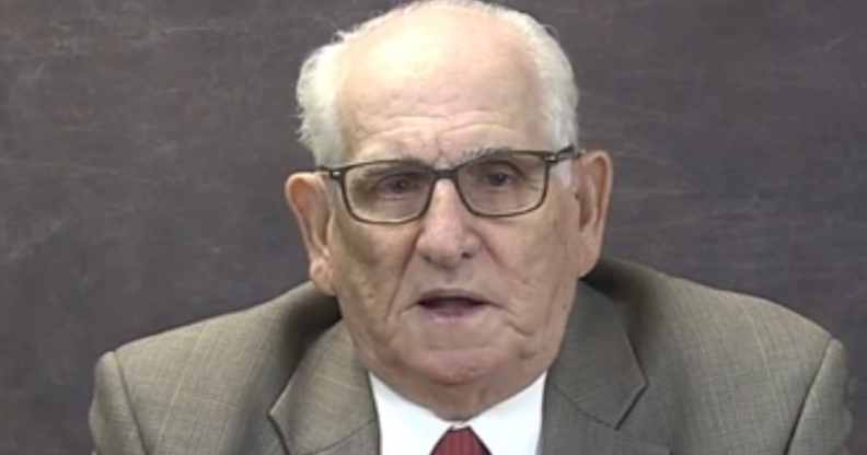 Dick Marston in a grey suit and red tie speaks to the camera against a grey background