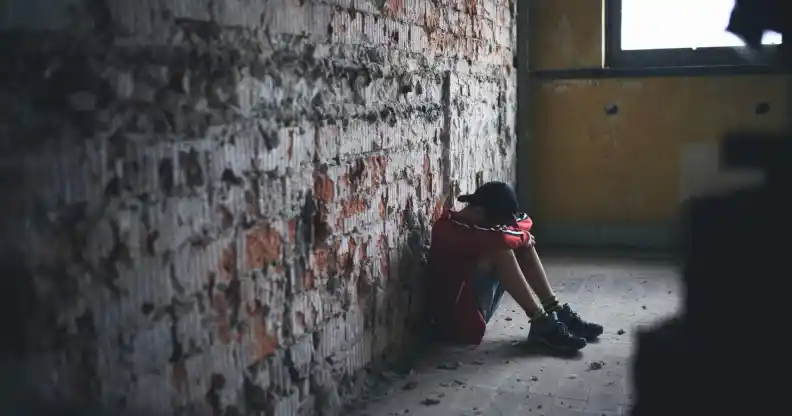 Sad and disappointed teenagers boy sitting indoors in abandoned building