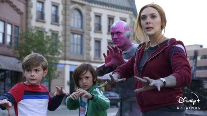 Superheros Wanda and Vision with their two young children, Billy and Tommy, all standing in a street with their hands raised, ready to attack