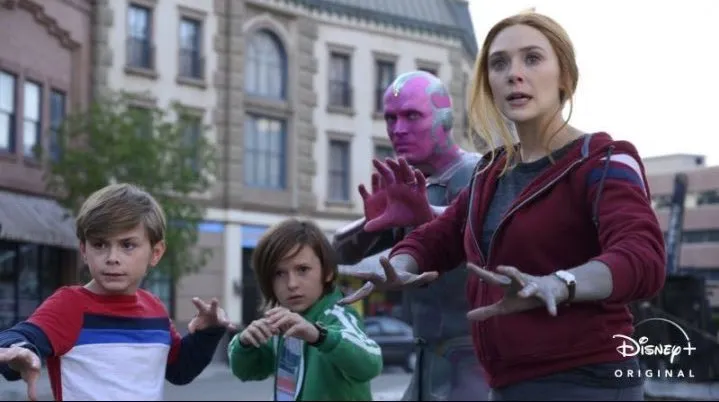 Superheros Wanda and Vision with their two young children, Billy and Tommy, all standing in a street with their hands raised, ready to attack