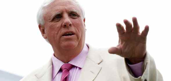 Jim Justice gestures with his hand in a white suit, pink shirt and pink tie outside