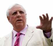 Jim Justice gestures with his hand in a white suit, pink shirt and pink tie outside