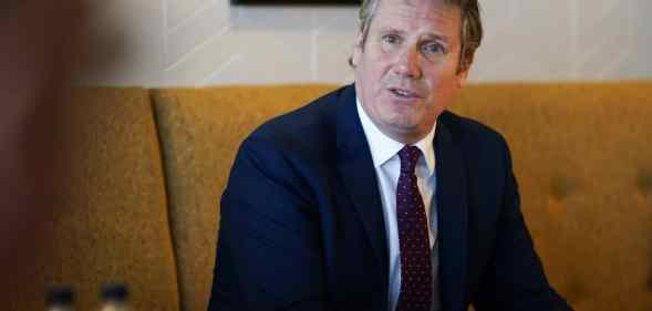 Keir Starmer watches on sat in a cushioned chair wearing a suit