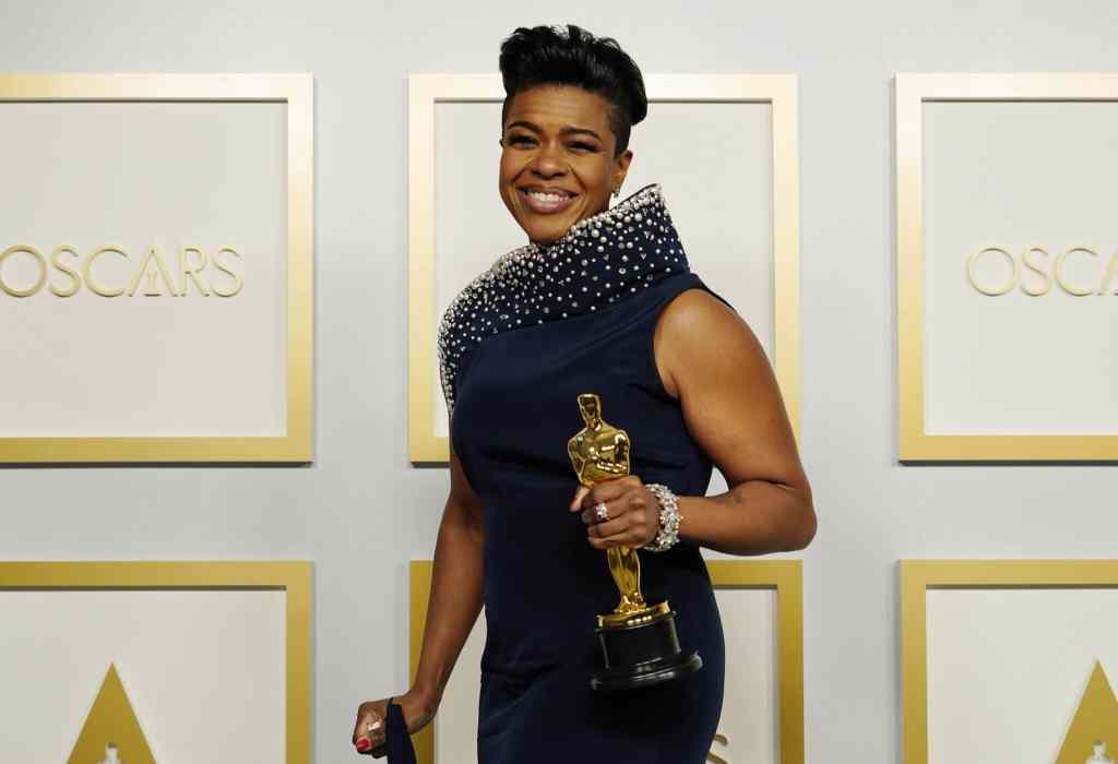 Mia Neal triumphantly holds her Oscar award in a navy dress on the Oscars red carpet