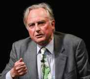 Richard Dawkins gestures while wearing a grey suit and green tie