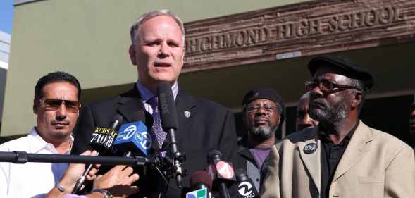 Chris Magnus, a cop in a suit, speaking into reporters' microphones