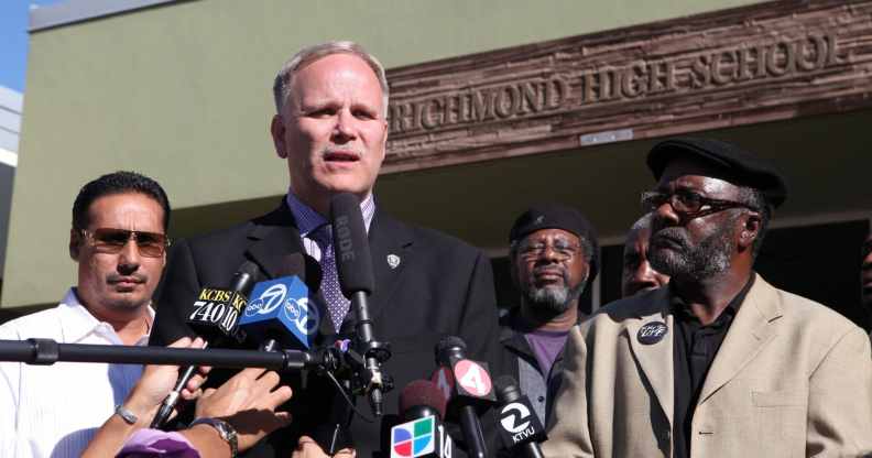 Chris Magnus, a cop in a suit, speaking into reporters' microphones