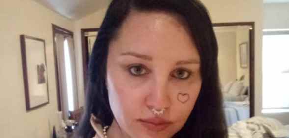 Amanda Bynes with a heart-shaped tattoo on her cheek looks to the camera in her bedroom