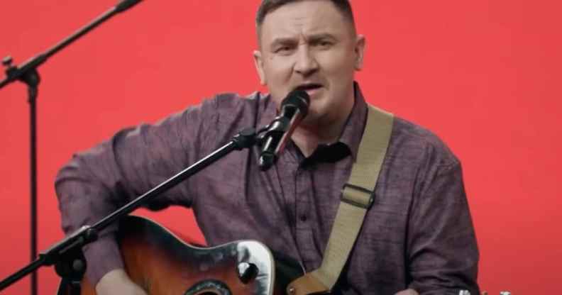 Dmitry Butakov sings while strumming the guitar against a red background