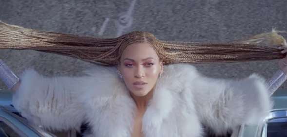 Beyoncé, from above, hanging out of a car window and holding her braids out to the side