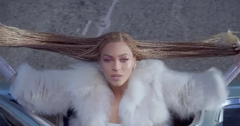 Beyoncé, from above, hanging out of a car window and holding her braids out to the side