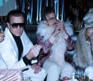 Ewan McGregor as Halston, sat with a woman, a man in a feather boa and another man in a mesh top