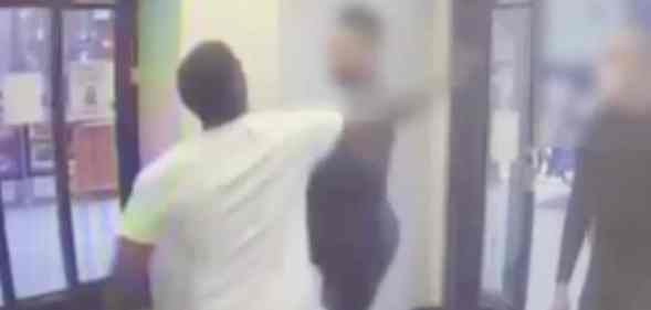 A man in a white tee shirts swings his fist at a man at the entrance of a drugstore