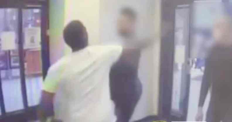 A man in a white tee shirts swings his fist at a man at the entrance of a drugstore