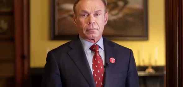 Charles Peruto stands in front of a painting in a red tie and dark suit