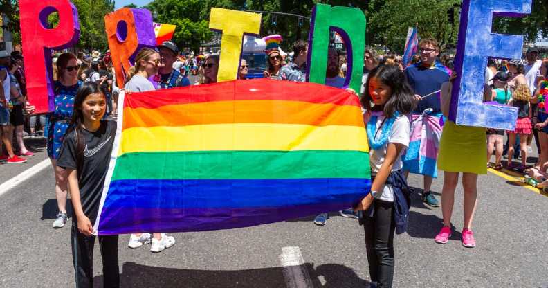 Two girls lead a segment of the parade with a rainbow flag followed by adults with the word 'PRIDE' during the Portland Pride Parade