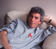 Patrick O'Connell sitting on his bed in a blue shirt and red ribbon