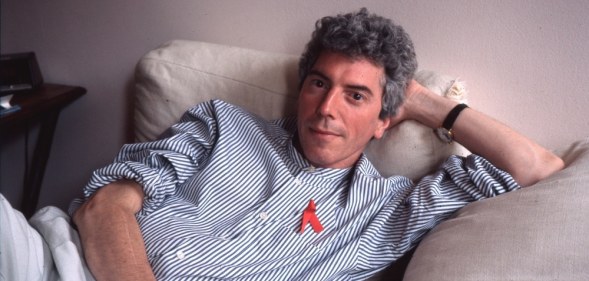 Patrick O'Connell sitting on his bed in a blue shirt and red ribbon
