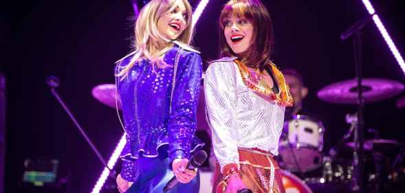 JoJo Desmond and Rhiannon Porter of ABBA MANIA, in costume while singing against one another's backs