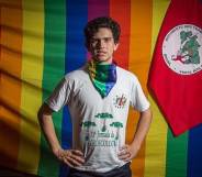 Lindolfo Kosmaski stands with his hands on his hips against the LGBT+ Pride and Landless Workers' Movement flags