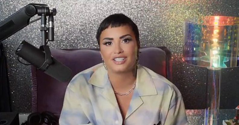 Demi Lovato speaks to the camera sat on a sofa wearing a plaid shirt