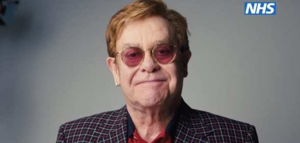 Elton John smiles against a grey background