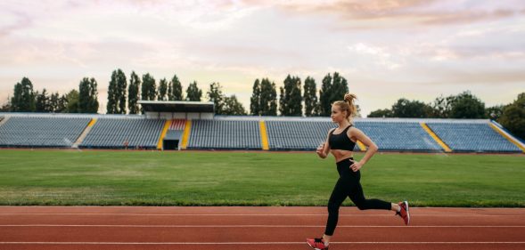 Female runner in sportswear jogging, training on stadium. Woman doing stretching exercise before running on outdoor arena