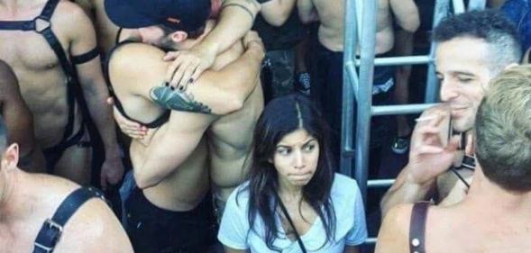 A young woman in a v-neck t-short surrounded by leather-clad, shirtless men