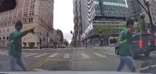 The view of a street crossing from a vehicle's dash cam, showing a man in a green hoodie and blue jeans walk past