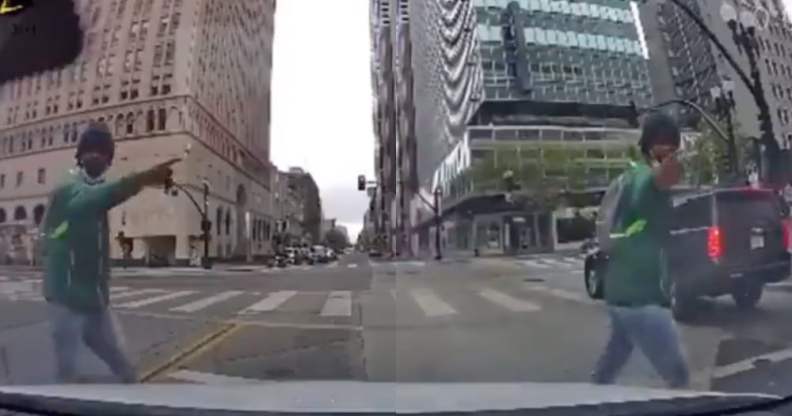 The view of a street crossing from a vehicle's dash cam, showing a man in a green hoodie and blue jeans walk past