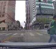 The view of a street crossing from a vehicle's dash cam, showing a man in a green hoodie and blue jeans walk past