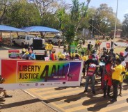 Holding a banner that says "Liberty, Justice Four All", Malawi Pride-goers walk along a street