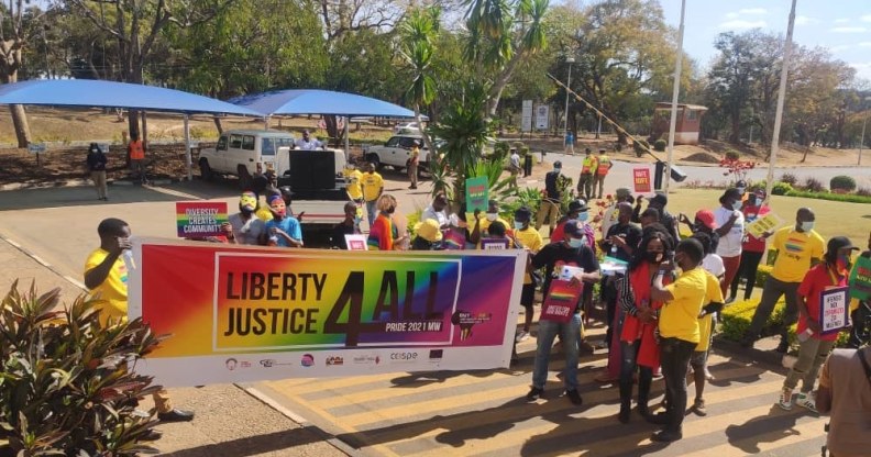 Holding a banner that says "Liberty, Justice Four All", Malawi Pride-goers walk along a street