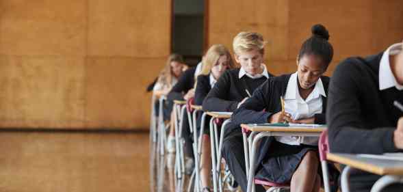 Teenage Students In Uniform Sitting Examination In School Hall