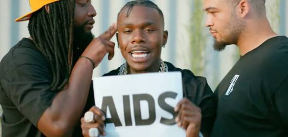 DaBaby holds up a sign with the word "AIDS" on it