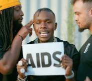 DaBaby holds up a sign with the word "AIDS" on it
