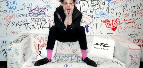 Yungblud, real name Dominic Harrison, visits Music Choice in 2019 and poses against a background of graffiti while sitting on a sofa