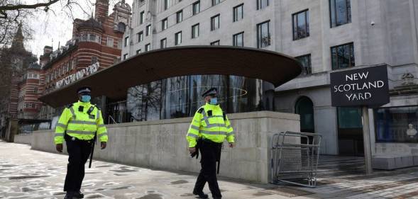 Police officers wearing face coverings due to Covid-19 walk past New Scotland Yard, the headquarters of the Metropolitan Police Service