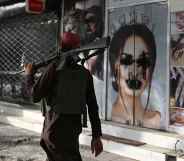 A Taliban fighter walks past a beauty salon with images of women defaced.