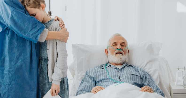 A family stands around their grandfather as he lies dying in a hospital bed