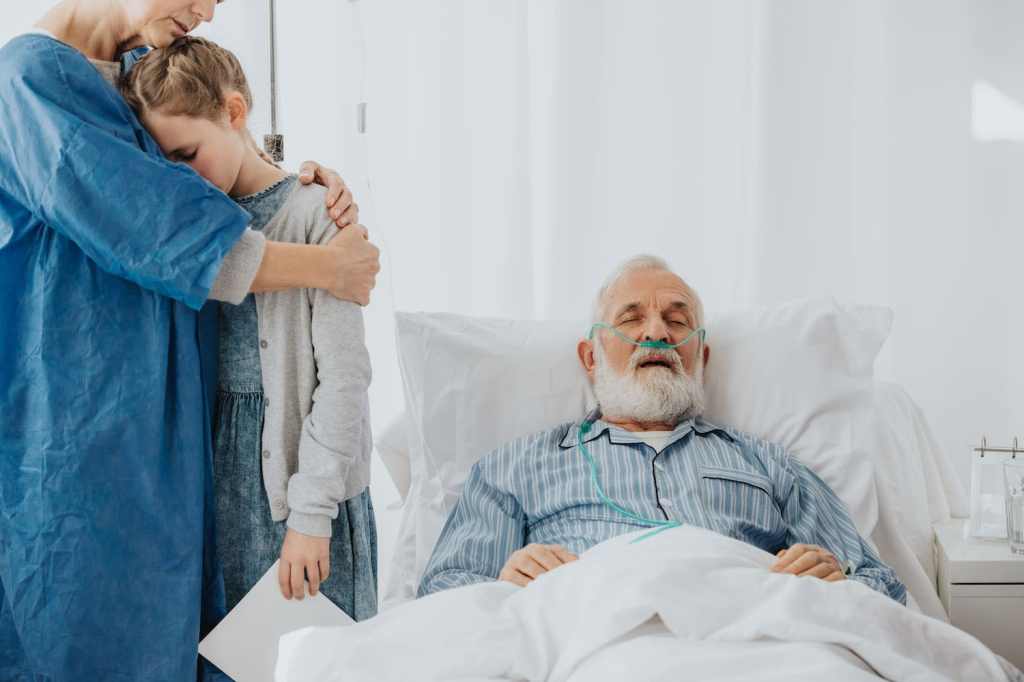 A family stands around their grandfather as he lies dying in a hospital bed