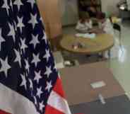 American flag hangs in the foreground of a classroom as two people sit at a table in the background