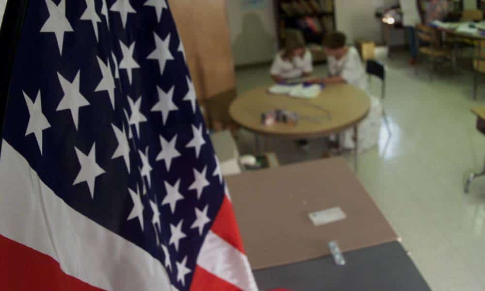 American flag hangs in the foreground of a classroom as two people sit at a table in the background