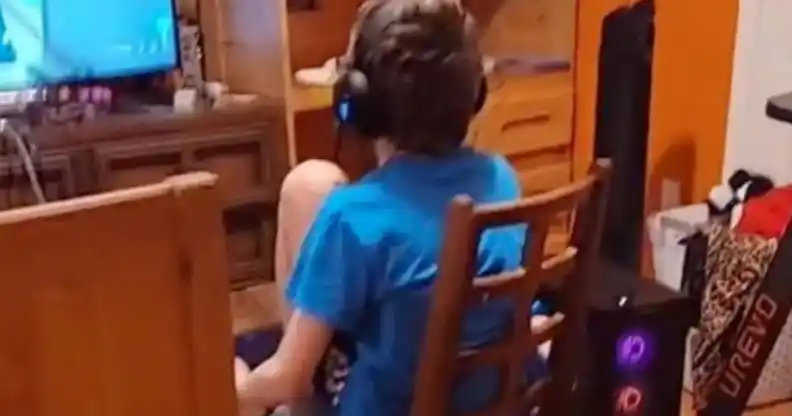 A 12-year-old sits on a wooden chair playing video games